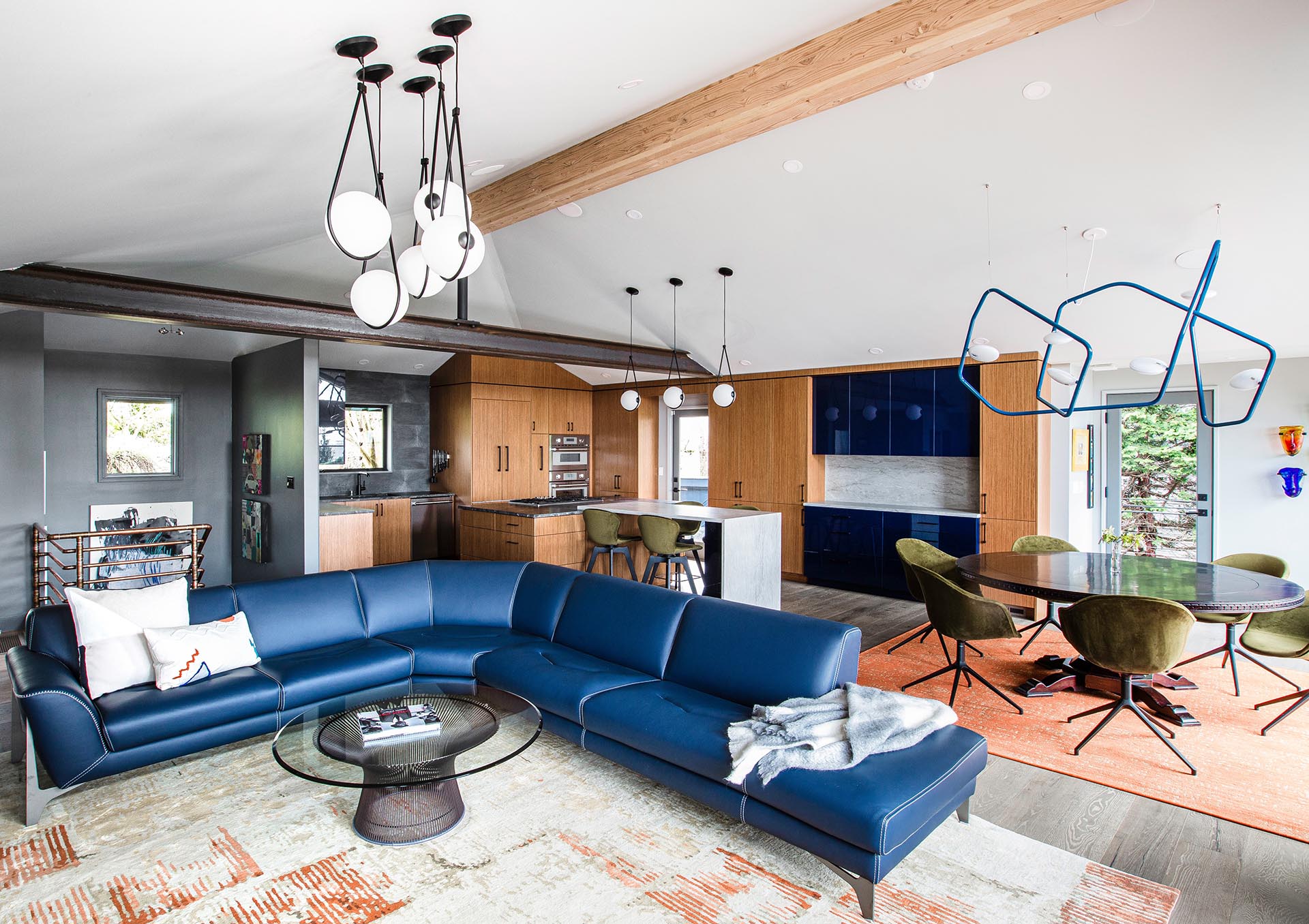 Renovated open concept living room with exposed wood and steel beams and natural teak kitchen cabinets with blue accents.