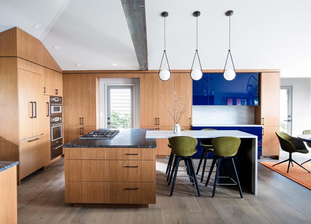 Redesigned kitchen with bold blue lacquer accent cabinets a mix earthiness of rift-cut teak cabinetry, and green stools.