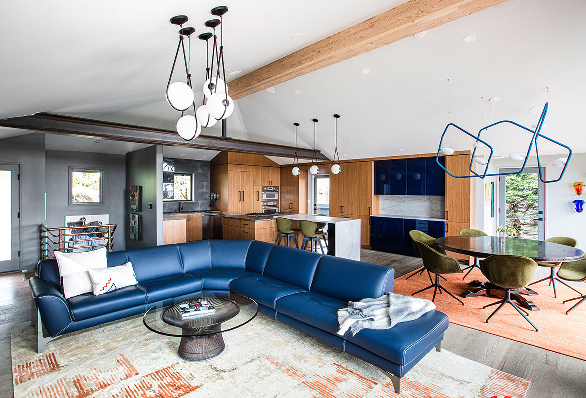 Renovated open concept living room with exposed wood and steel beams and natural teak kitchen cabinets with blue accents.