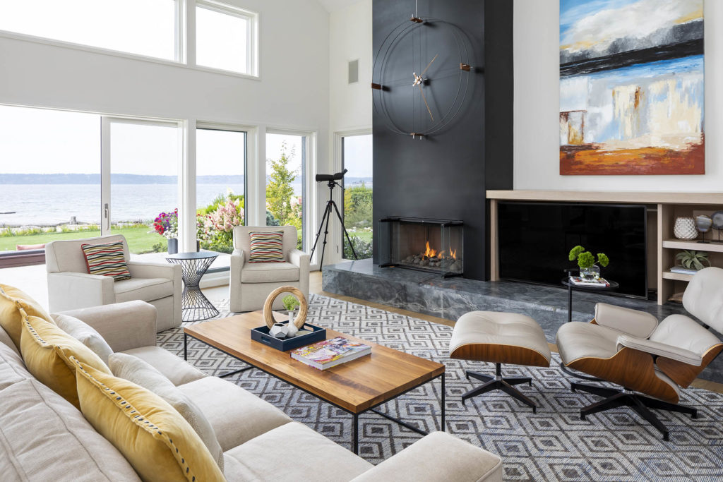 Renovated transitional style living room with black fireplace, large windows allowing natural light and beautiful ocean views