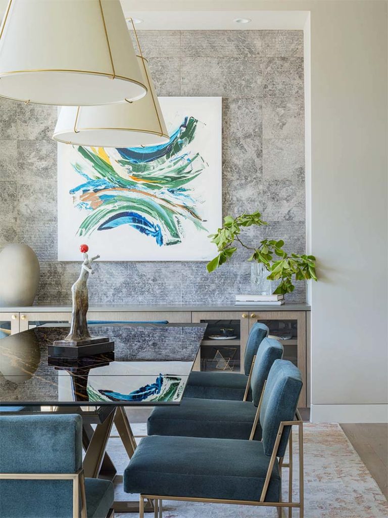 Newly designed dining room in Kirkland with glass dining table, Thayer Coggin blue and brass chairs and textured marble wall.