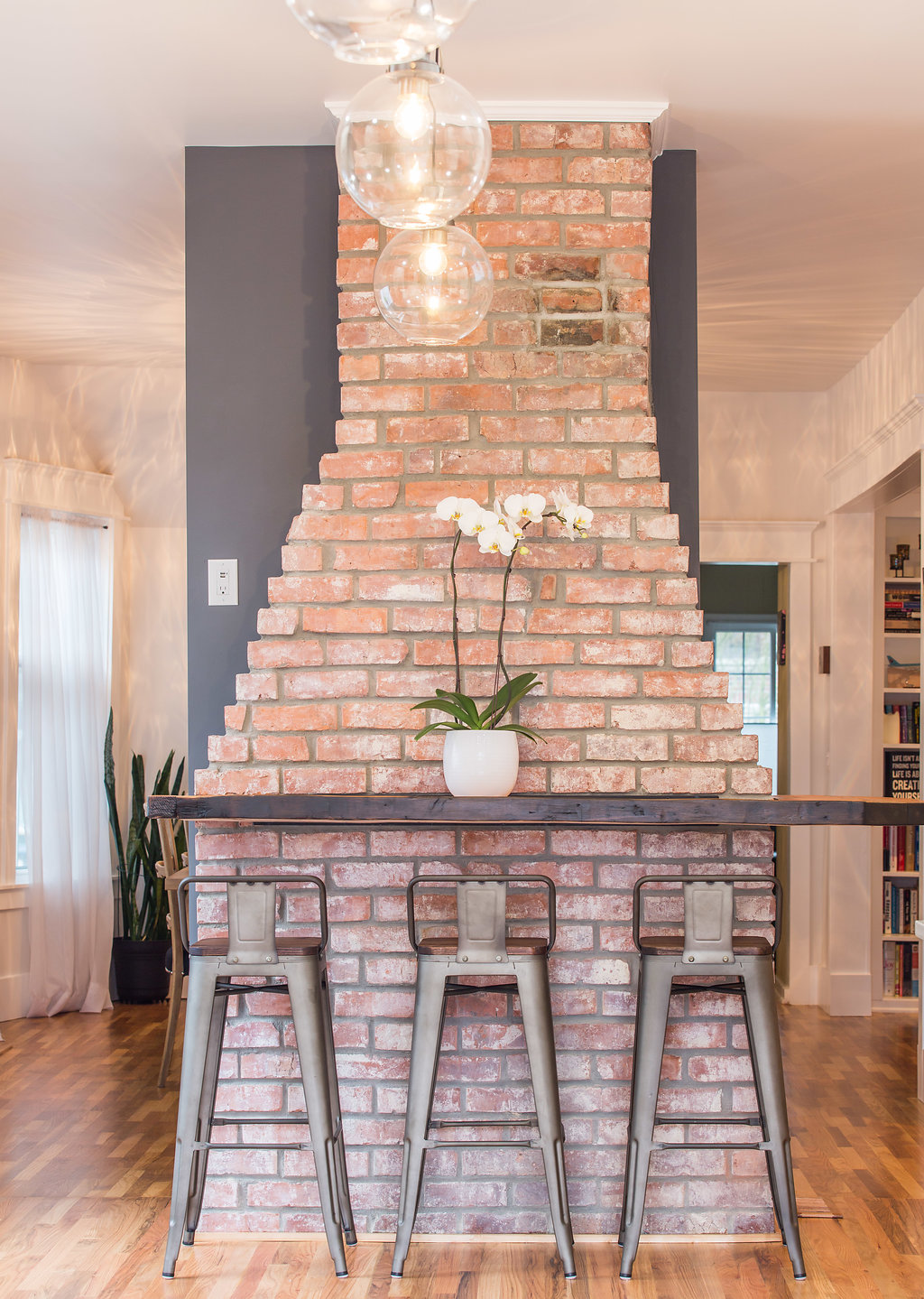Exposed brick chimney repurposed as a bar counter with wood plank shelf and stools