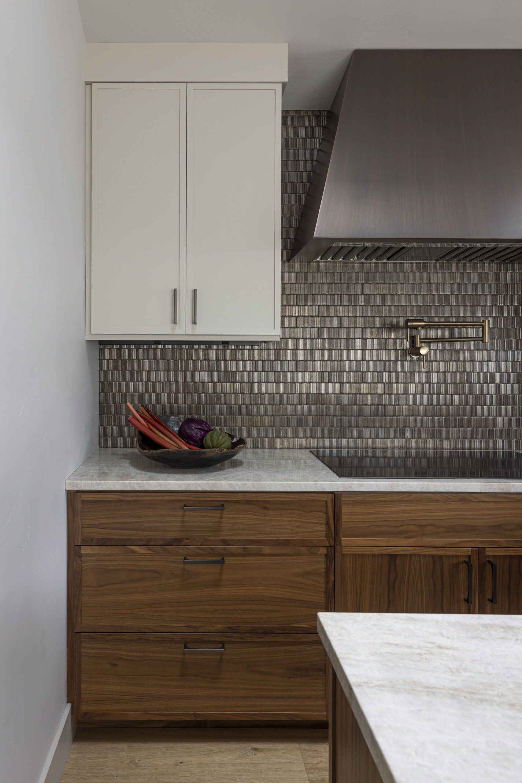 Kitchen with walnut cabinetry, metallic tile backsplash, and brass wall-mounted pot filler and copper hood