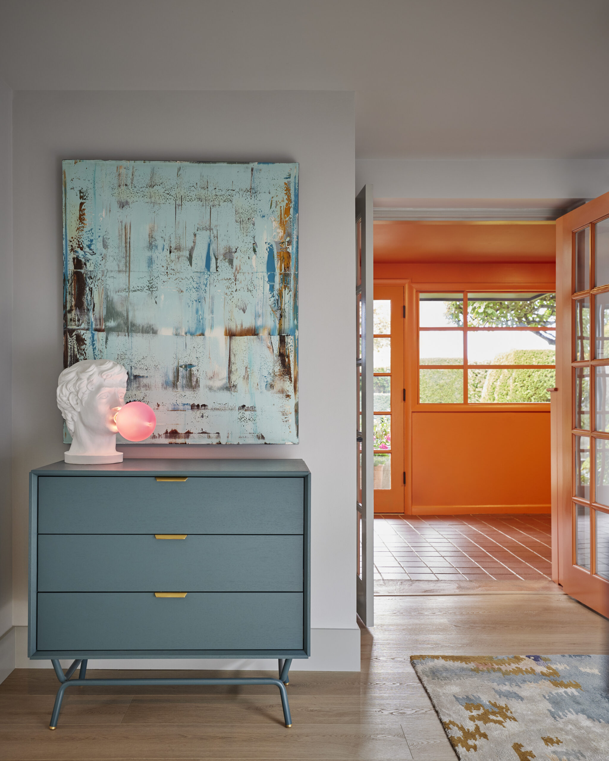 Entryway with blue dresser, abstract painting, and plaster bust lamp beside an orange-framed door